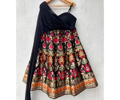 One Shoulder Steal everyone's heart and attention by wearing this dazzling black lehenga made of banarasi silk material embellished with all-over zari And Mina weaving work. This beautiful lehenga comes with a stylish crop top made of georgette material in black color which is featured with an attached pleated dupatta style and sweat heart shape spaghetti crop top.  Buy this style of Black Royal Blue And Green color lehenga that will give you a beautiful glamour look after you wear it. Team it w Traditional Black Choli With Dupatta, Traditional Black Choli With Zari Work, Designer Black Lehenga With Traditional Drape, Black Choli With Traditional Drape For Reception, Black Lehenga With Resham Embroidery, Traditional Black Unstitched Lehenga, Traditional Unstitched Black Lehenga, Black Unstitched Lehenga With Traditional Drape, Designer Unstitched Black Lehenga