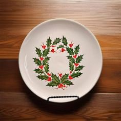 a white plate with holly and red berries painted on the side sitting on a wooden table