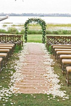 an outdoor ceremony setup with chairs and flowers on the aisle, along with greenery