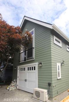 a green house with an air conditioner on the front and second story balcony above it