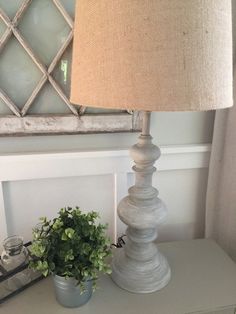 a white table with a lamp and some plants on it