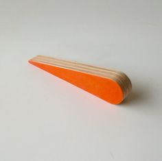 an orange piece of wood sitting on top of a white table next to a wooden stick