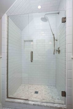 a walk in shower sitting next to a white tiled wall and floor with a glass door