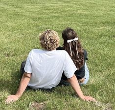 two people sitting on the grass looking at an airplane