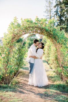 a bride and groom standing in front of an arch covered with greenery at their wedding