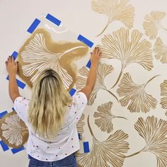 a woman is painting a wall with gold leaf stencils