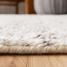 a close up of a white rug on a wooden floor with a chair in the background