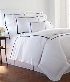 a bed with white sheets and blue trimmings in a room next to a table