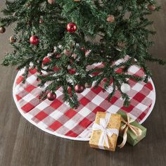 a small christmas tree with presents under it on a checkered tablecloth and wooden floor