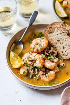 a bowl filled with shrimp and bread on top of a white table next to two glasses of water