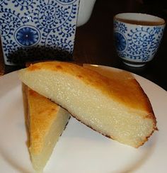 a piece of cake on a white plate with blue and white china cups in the background