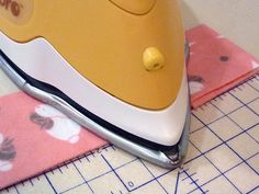 a yellow and white electric iron sitting on top of a pink mat next to a ruler