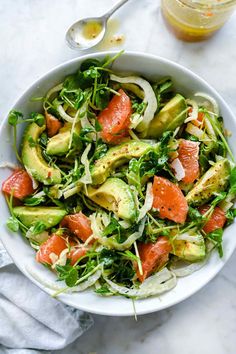 a white bowl filled with salad and topped with avocado, salmon and spinach