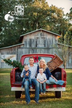 a family sitting in the back of a red pickup truck with christmas decorations on it