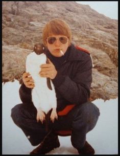 a man in black jacket and sunglasses holding up a white fish on top of snow covered ground