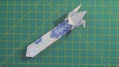 an origami airplane made out of money on a green cutting mat with scissors