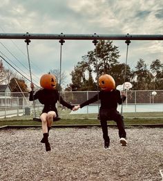 two people sitting on swings with pumpkin heads on their faces, one holding the other's hand