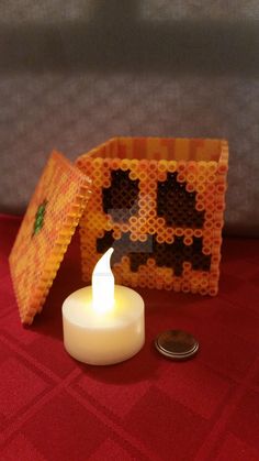 a lit candle sitting next to a piece of lego art that looks like a pumpkin