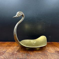 a metal bird sculpture sitting on top of a wooden table next to a black wall