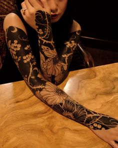 a woman is sitting at a table with her arm covered in black and white tattoos