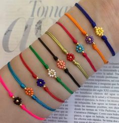 six different colored bracelets with beads and flowers on each one hand, sitting on top of an open book