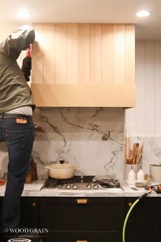 a man standing on top of a kitchen counter next to a stove top oven under a wooden cabinet