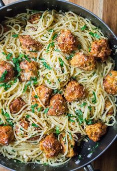 spaghetti with meatballs and parmesan cheese in a skillet on a wooden table