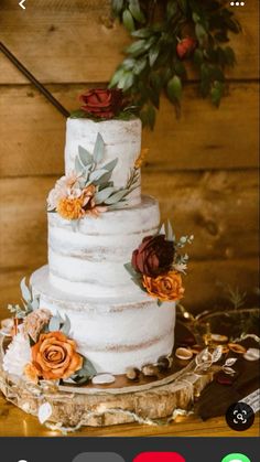 a three tiered cake with flowers on the top is displayed in front of a wooden background