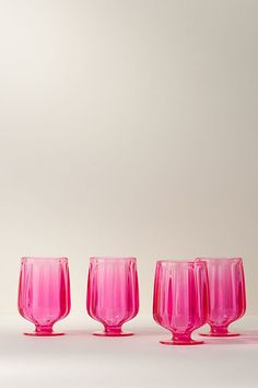 five pink wine glasses lined up in a row on a white surface with one empty