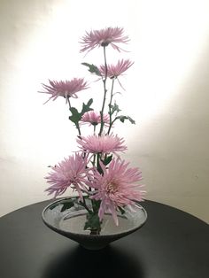 a vase with pink flowers in it sitting on a black table next to a white wall