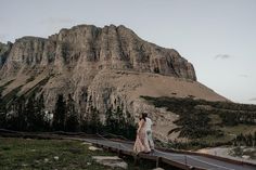 a man and woman standing on a bridge in front of a mountain