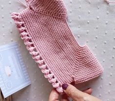 someone is holding up a pink knitted sweater with crochet details on it