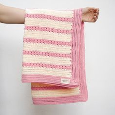 a person holding two crocheted blankets in their hands, one pink and the other white