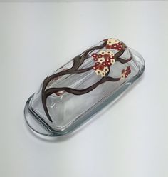 a glass vase with flowers and leaves on the bottom is sitting on a white surface