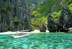 two boats are in the clear blue water near large rocks and green trees on either side