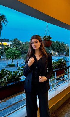 a woman standing in front of a window wearing black pants and a blazer jacket