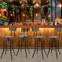 four stools in front of a bar with plants growing on the wall and overhead lights