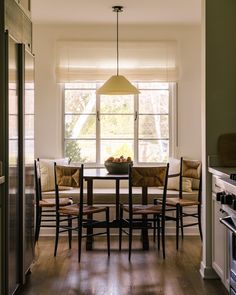 a dining room table with four chairs and a light hanging from the ceiling over it