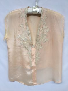 "1930s Vintage Peach sleeveless top with embroidered net lace collar and rosette. Lace is embroidered net with tropical leaves and flowers. It is set onto the neckline with zig zag around the motifs. It is not a mirror image as each side has it's own shape. The rosette is hand made of an ecru scallop trim that has been sewn into a spiral. Inside facing and front placket is hand stitched (original) Although the lace is older, it does not appear to be original to the piece. Tag/Label: N/A Material Vintage Lace Trim Camisole Top, Vintage Camisole Top For Daywear, Wedding Camisole Top With Lace Trim, Vintage Sleeveless Wedding Tops, Vintage Sleeveless Lace Top With Lace Trim, Vintage Lace V-neck Top, Vintage Sleeveless Tops For Daywear, Vintage Sheer Tops For Wedding, Vintage Lace Work Tops For Wedding