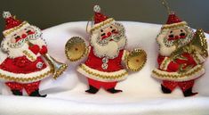 three santa claus ornaments are sitting on top of a white cloth covered tablecloth with gold trimmings