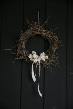 a wreath with white bows hanging on a black wooden wall next to a pair of scissors