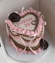 a heart shaped cake decorated with pink ribbons and hats on top of a white box