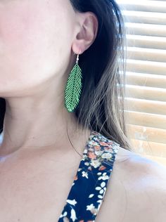 a close up of a person wearing large green leaves on their earring, with blinds in the background