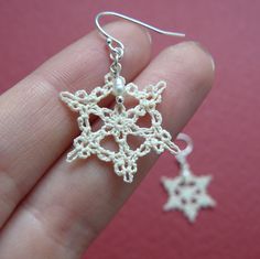 small white crochet snowflake earrings on someone's finger