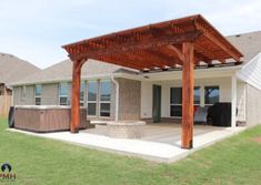 a covered patio with hot tub and grill in the back yard, surrounded by grass