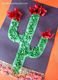 a cactus made out of paper on top of a piece of construction paper with red flowers