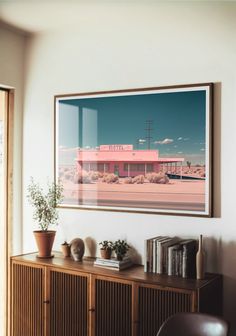 a framed photograph hangs on the wall next to a wooden cabinet with books and plants