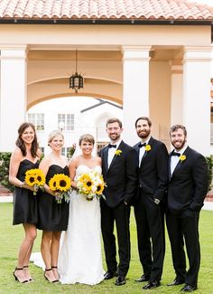 a group of people standing next to each other in front of a building with sunflowers