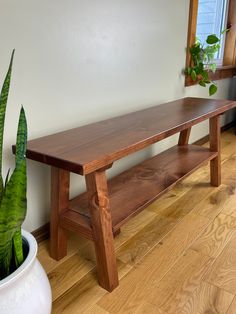 a wooden bench sitting on top of a hard wood floor next to a potted plant