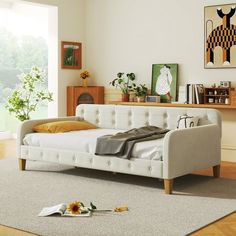 a white day bed sitting on top of a wooden floor next to a dresser and window